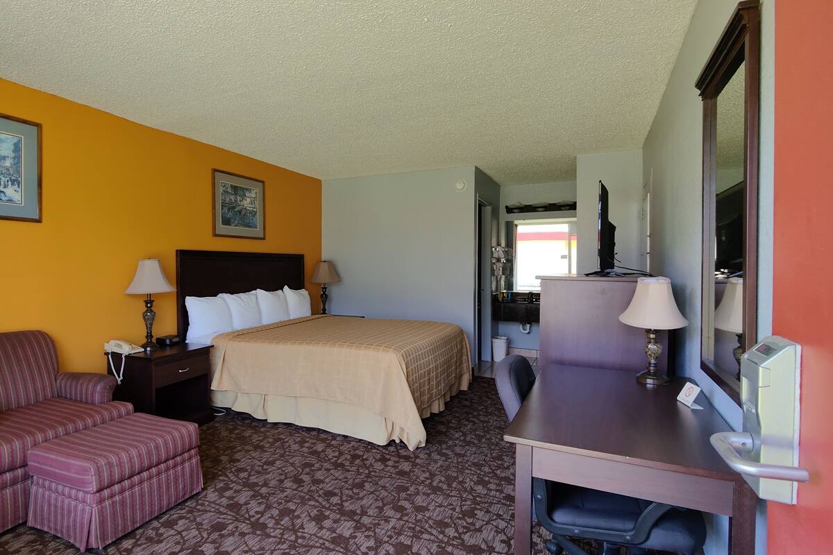 A hotel room with a bed, a desk, a chair, and two paintings on the wall.