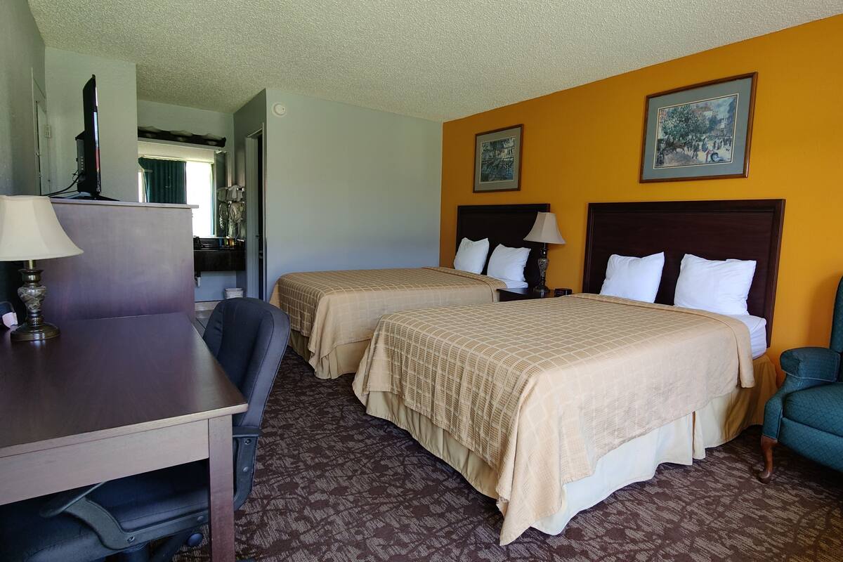 A hotel room with two beds, a desk, a chair, and a television.