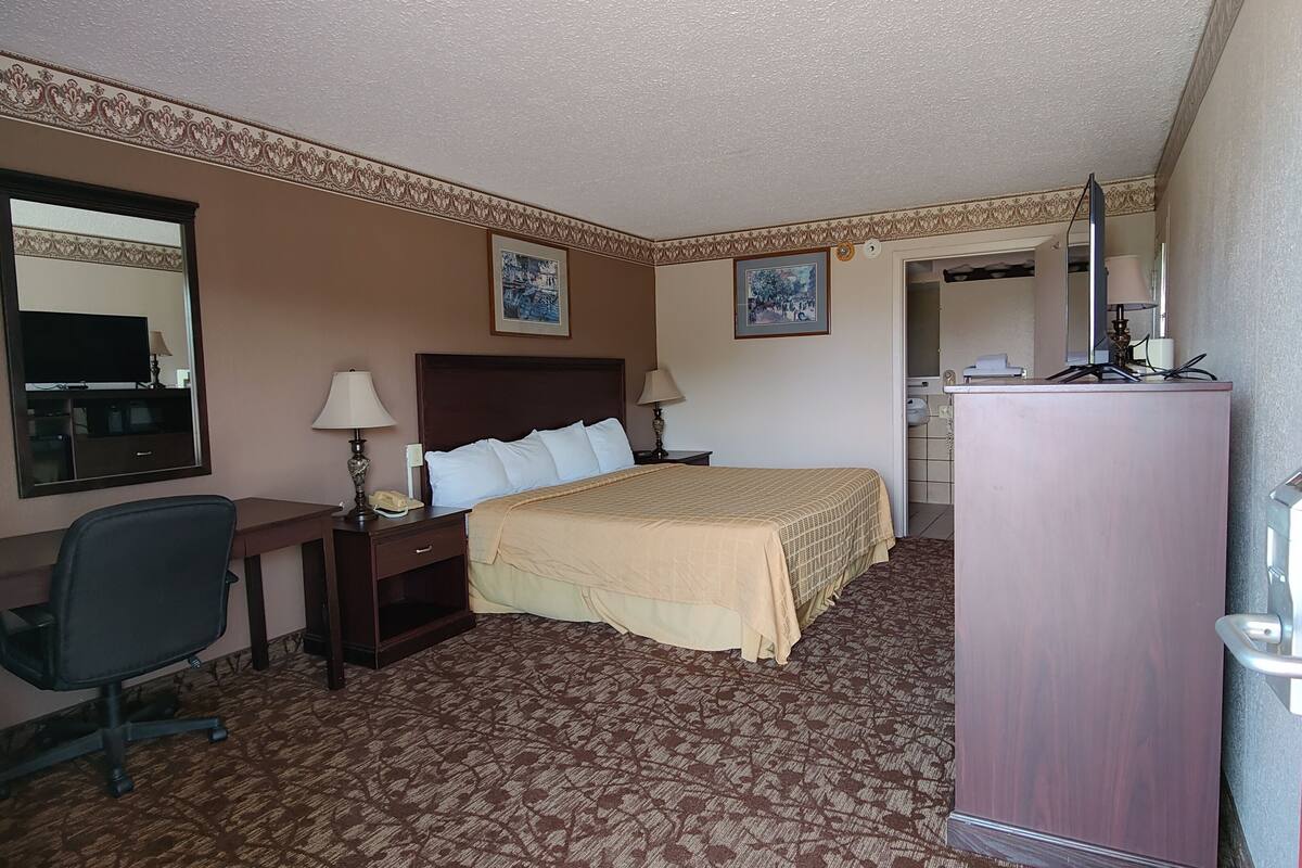 A hotel room with a bed, desk, chair, and a wardrobe.