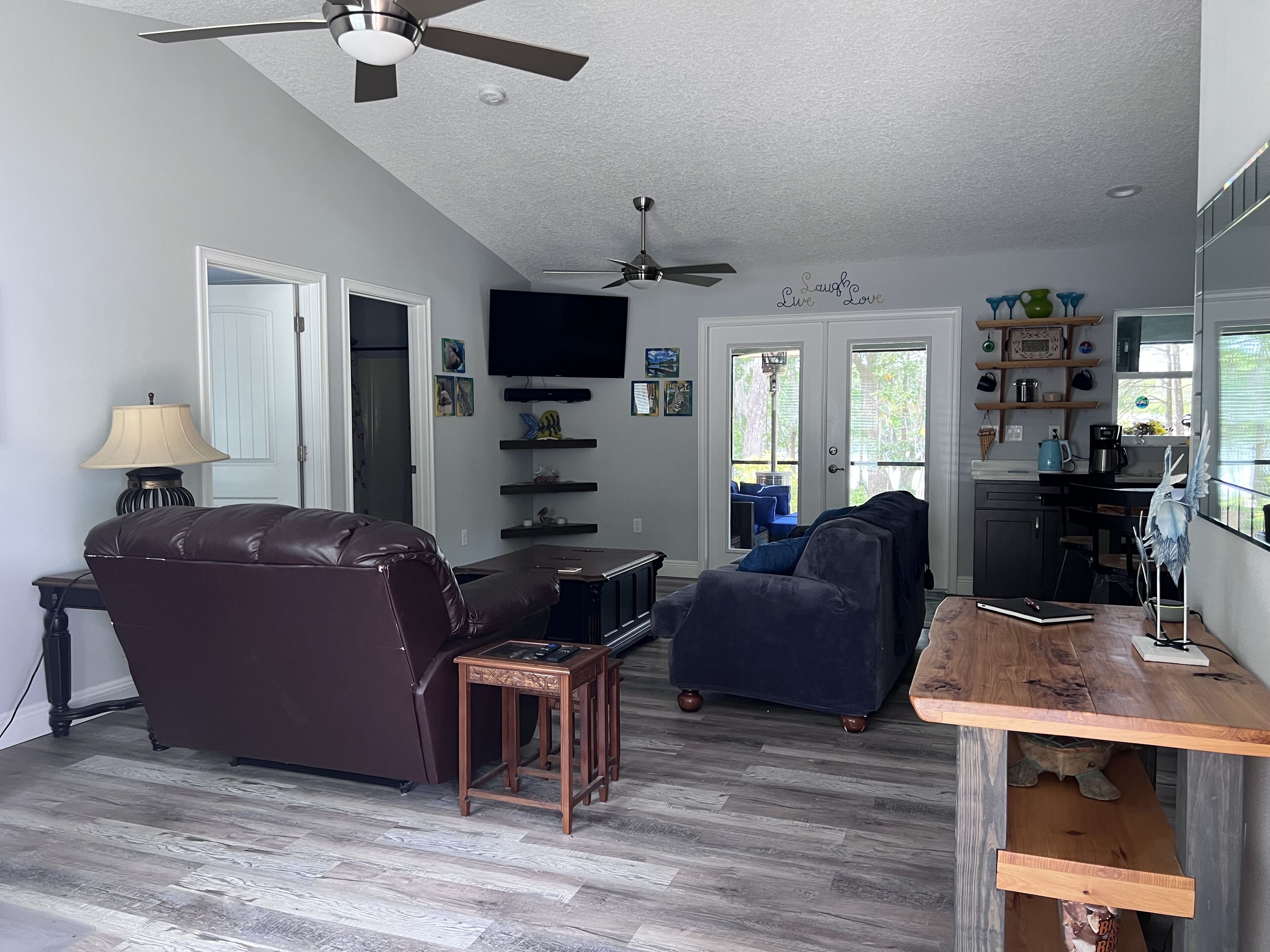 A spacious living room with a brown leather sofa, a blue armchair, a wooden coffee table, and a ceiling fan.