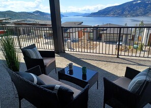 A balcony with wicker furniture, a table with two mugs, and a view of a lake and mountains. - Beautiful 2 bed 2 bath with incredible lake view!! (Lake Country)
