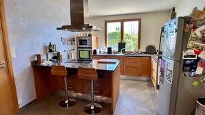 A modern kitchen with a central island, bar stools, a built-in oven, and a refrigerator with magnets. - House with garden in Provence (Valréas)