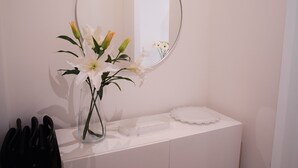 Une coiffeuse blanche avec un miroir rond, un vase de fleurs blanches et un plateau orné d’une bordure en dentelle.