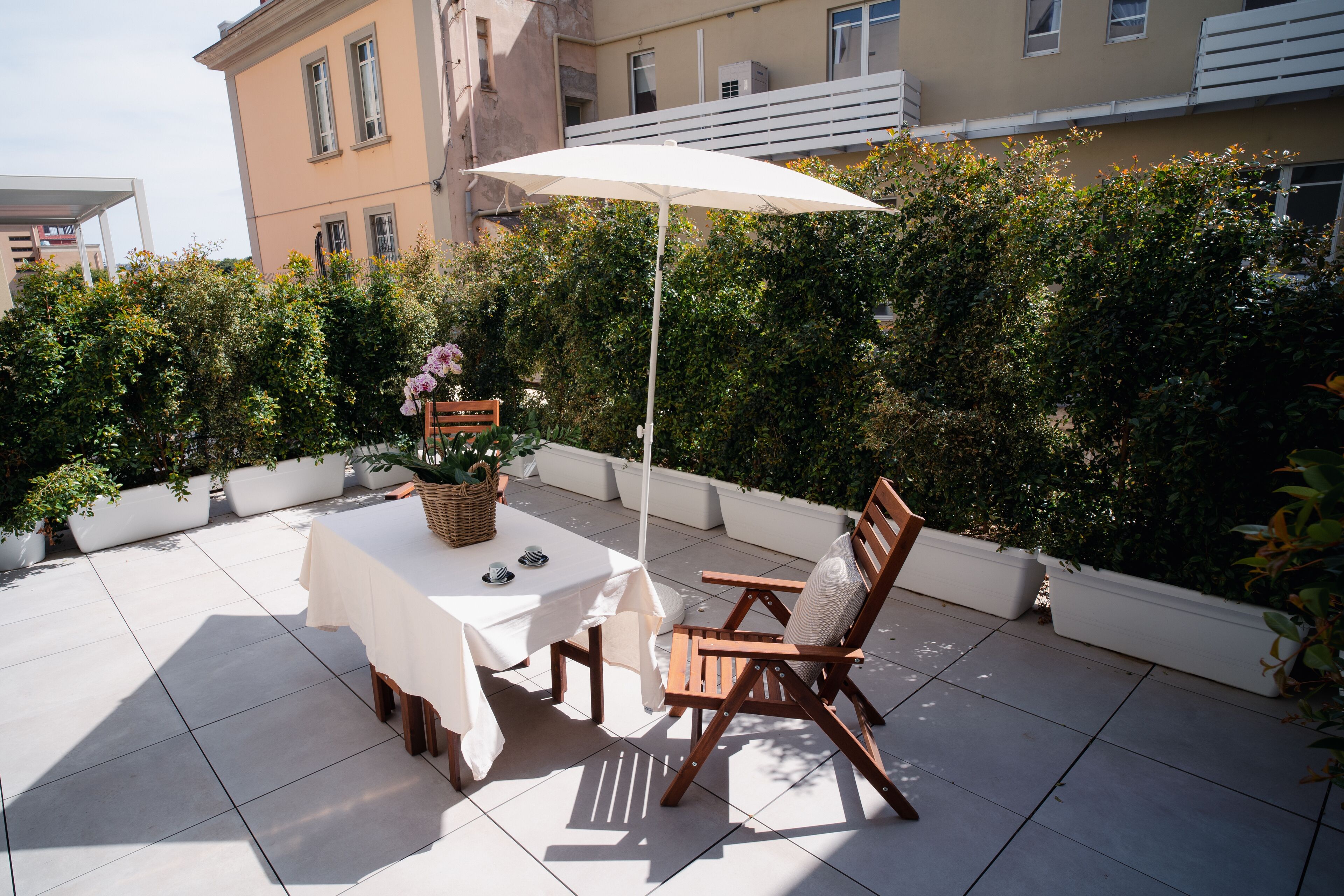 An outdoor patio with a table and chairs, a white umbrella, and potted plants.