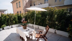 Une terrasse extérieure avec une table et des chaises, un parasol blanc et des plantes en pot.