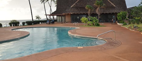A swimming pool with a curved design, a building with a sloped roof, and palm trees.