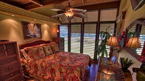 Una camera da letto con un letto grande, una ventola a soffitto, un comò in legno, una scrivania con una lampada e una finestra con persiane.