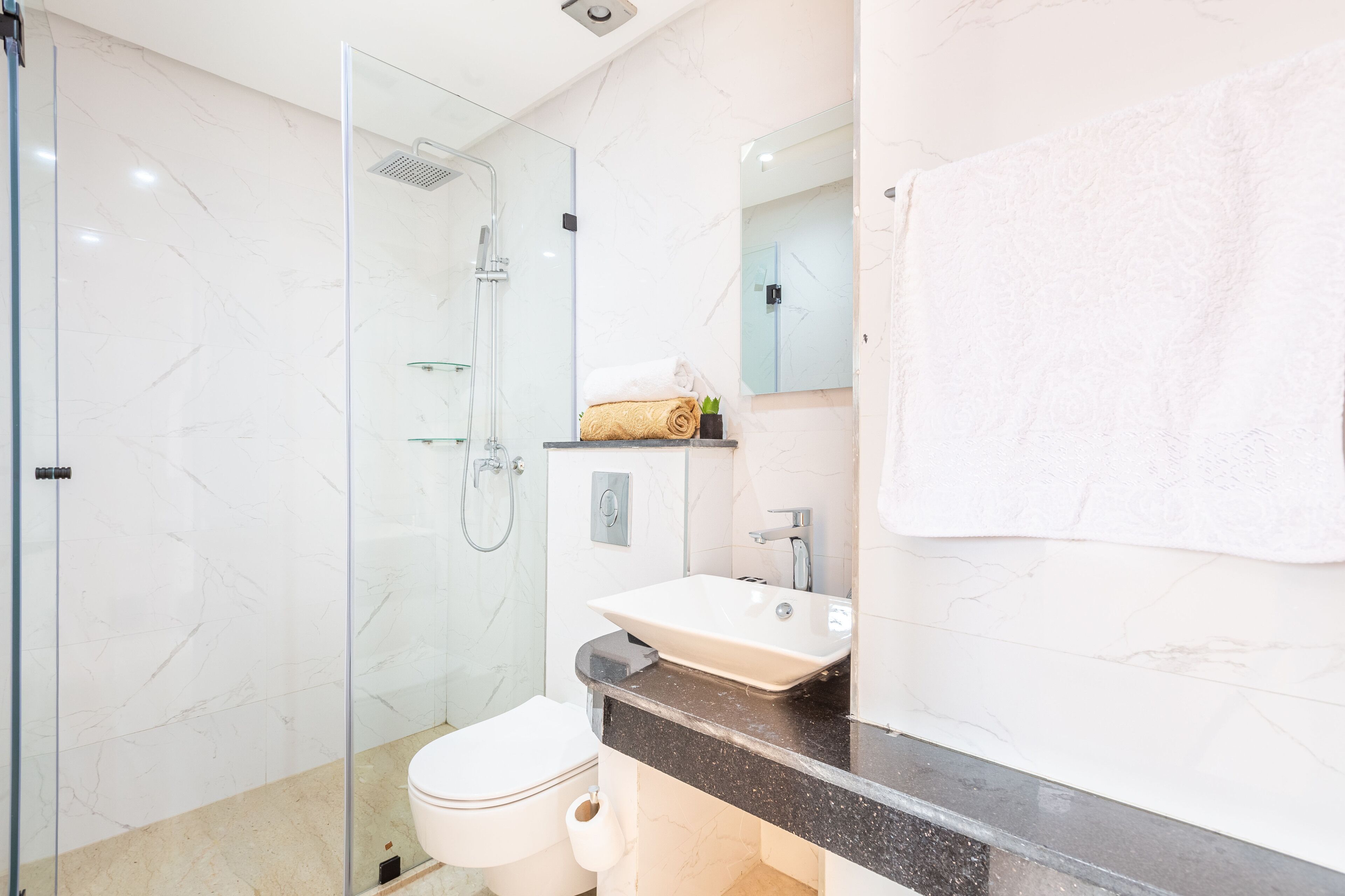 A modern bathroom with a glass-enclosed shower, a white toilet, and a sink with a marble countertop.