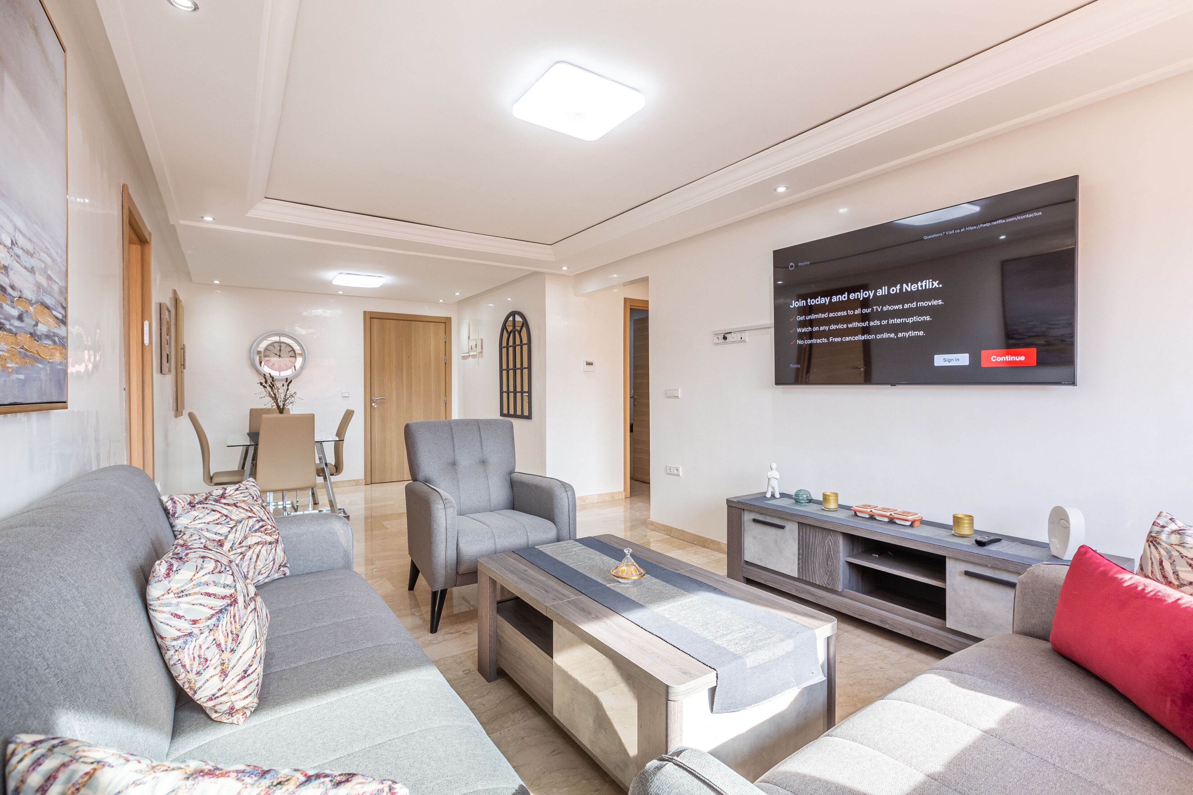 A modern living room with a sofa, armchair, coffee table, and a flat-screen TV mounted on the wall.