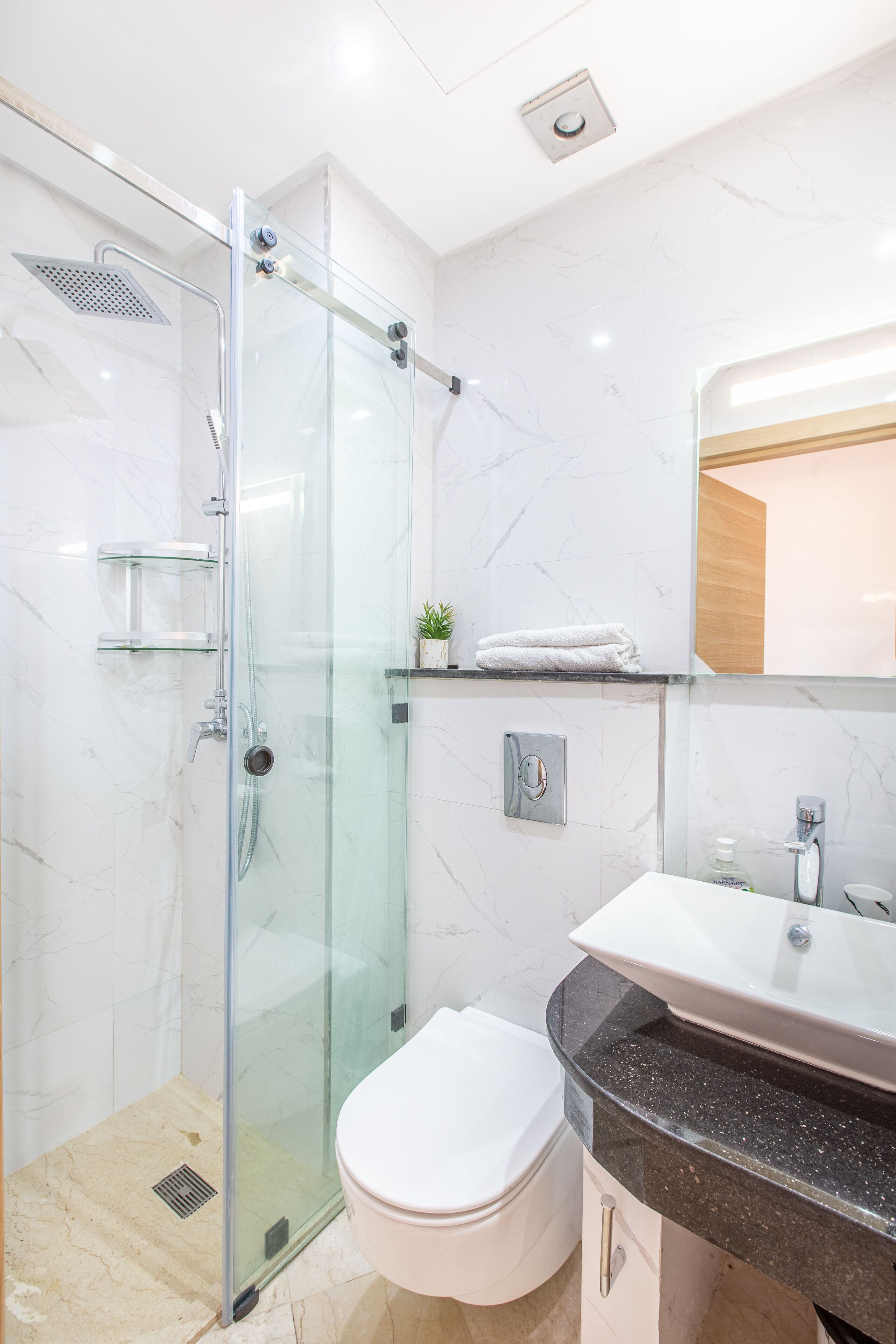 Un baño moderno con cabina de ducha de vidrio, inodoro blanco y lavamanos con encimera de mármol.