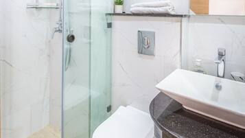 Un baño moderno con cabina de ducha de vidrio, inodoro blanco y lavamanos con encimera de mármol.