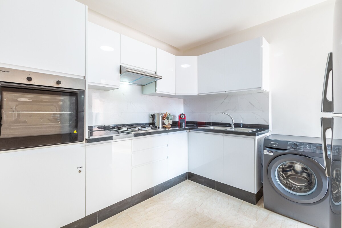 A modern kitchen with white cabinets, a built-in oven, a gas stove, a sink, and a front-loading washing machine.