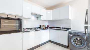 Una cocina moderna con gabinetes blancos, horno empotrado, estufa a gas, lavamanos y lavadora de carga frontal.