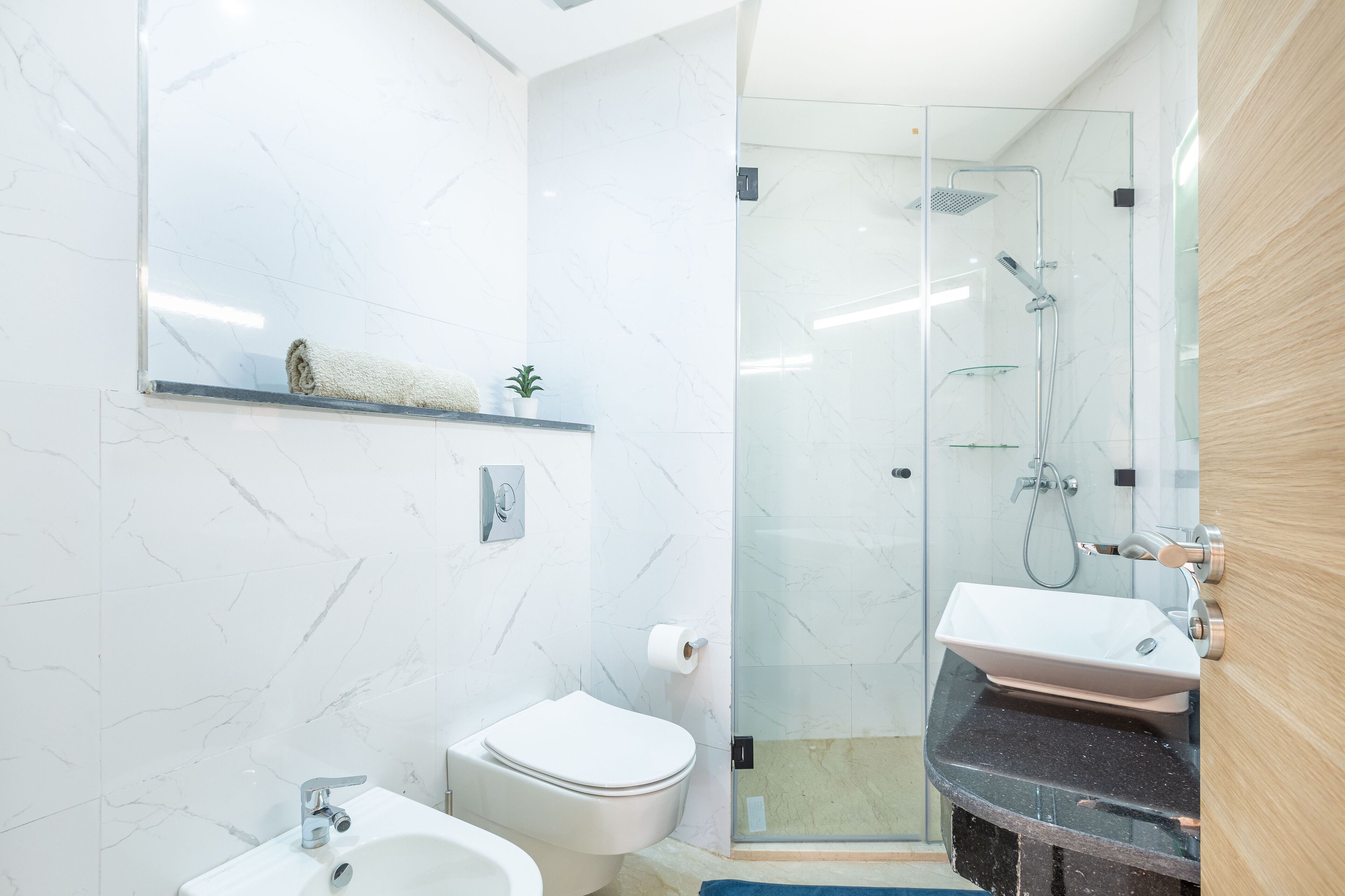A modern bathroom with a glass-enclosed shower, a white toilet, and a sink with a marble countertop.