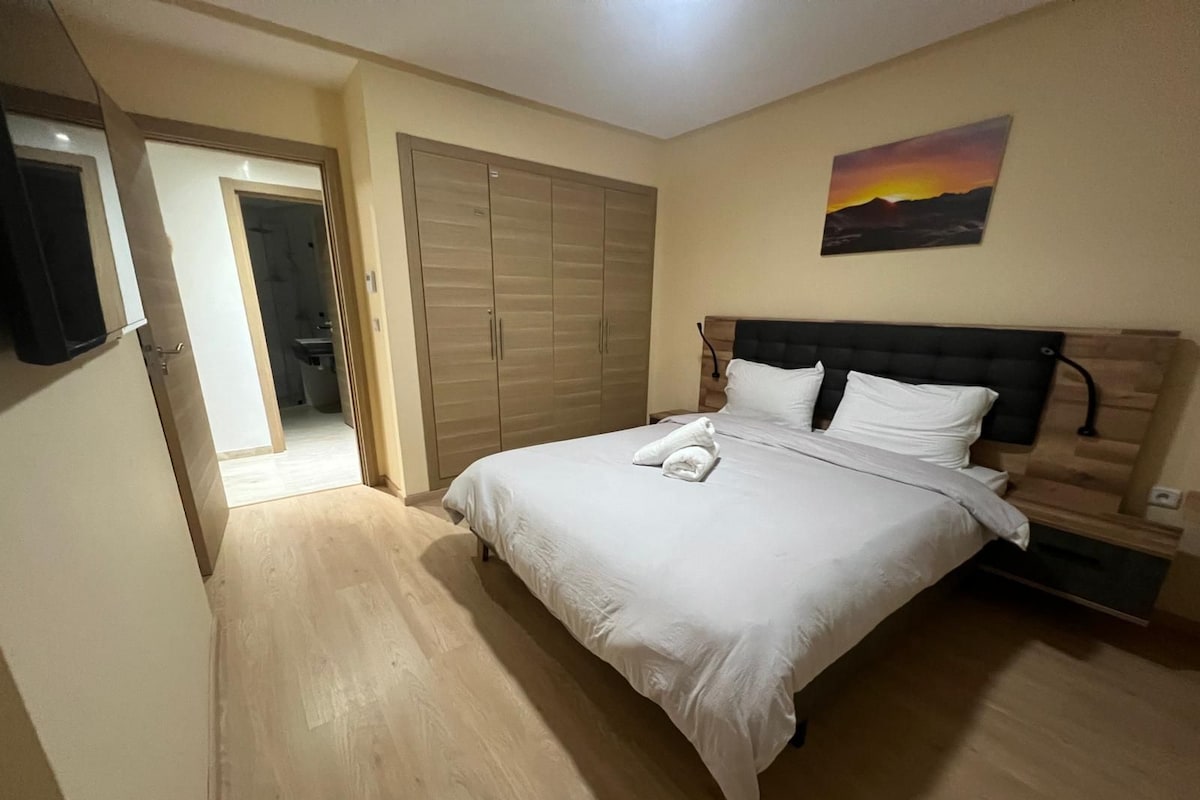 A bedroom with a bed, a wardrobe, a painting, and a door leading to another room.