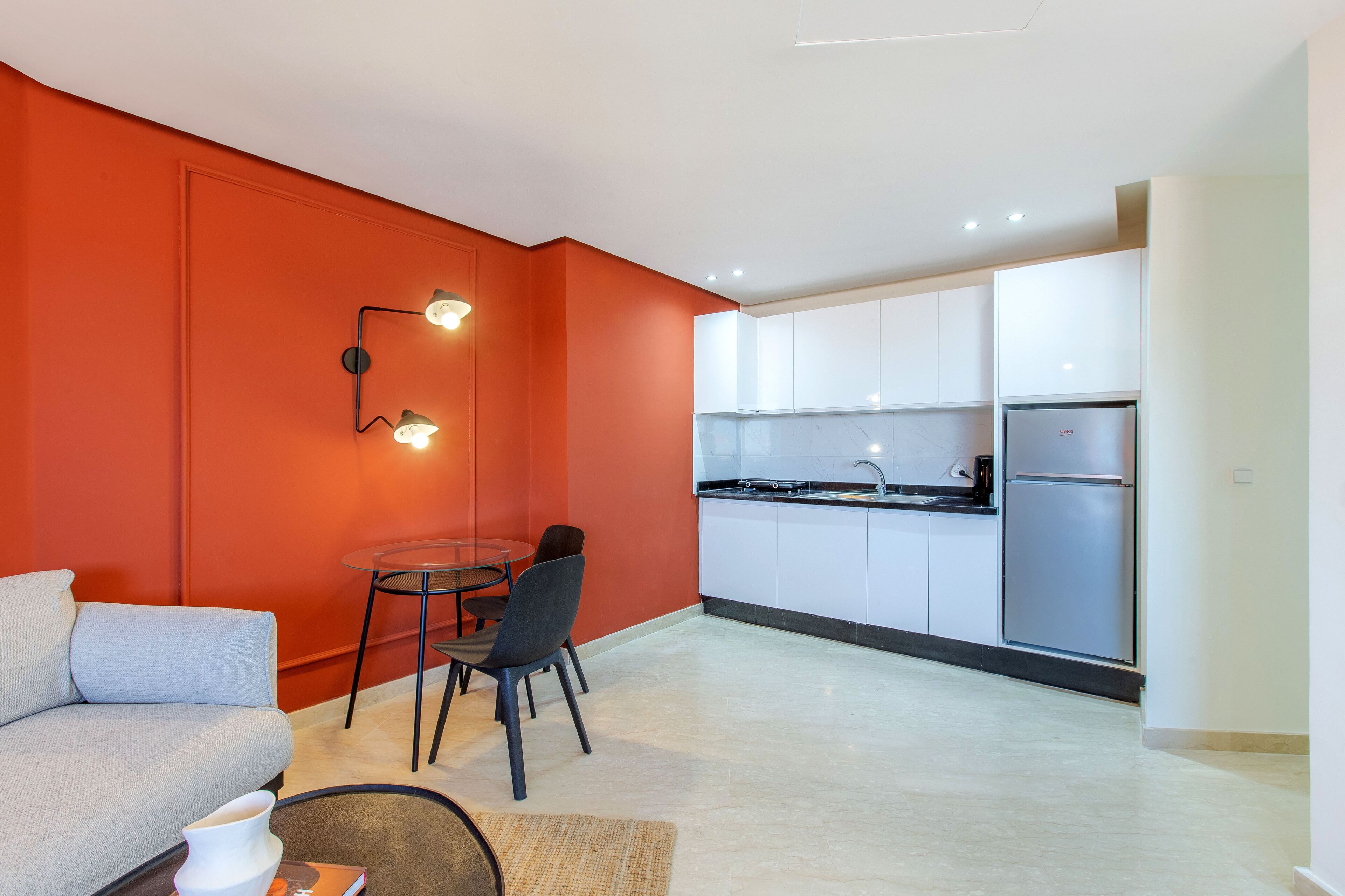 A modern kitchen with white cabinets, a stainless steel refrigerator, and a dining area with a table and chairs.