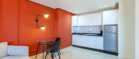 A modern kitchen with white cabinets, a stainless steel refrigerator, and a dining area with a table and chairs.
