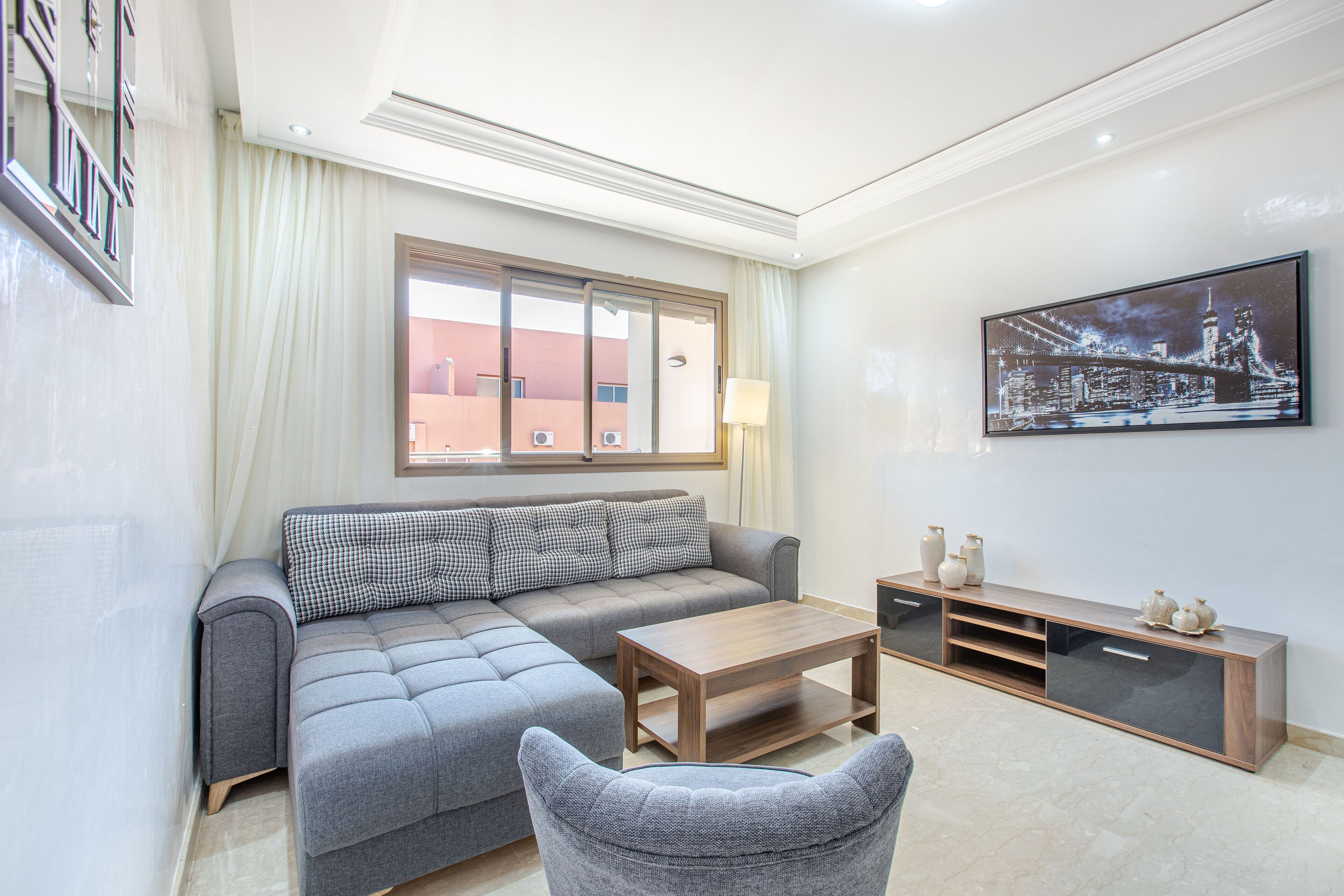 A modern living room with a sofa, a coffee table, a TV stand, and a large window.