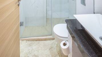 A modern bathroom with a glass shower enclosure, a toilet, a sink with a black countertop, and a white marble wall.