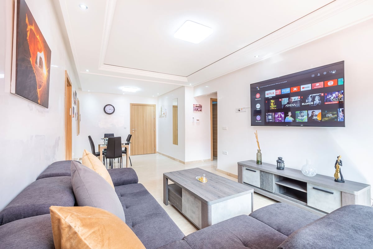 A modern living room with a grey sofa set, a coffee table, and a flat-screen TV displaying various streaming services.