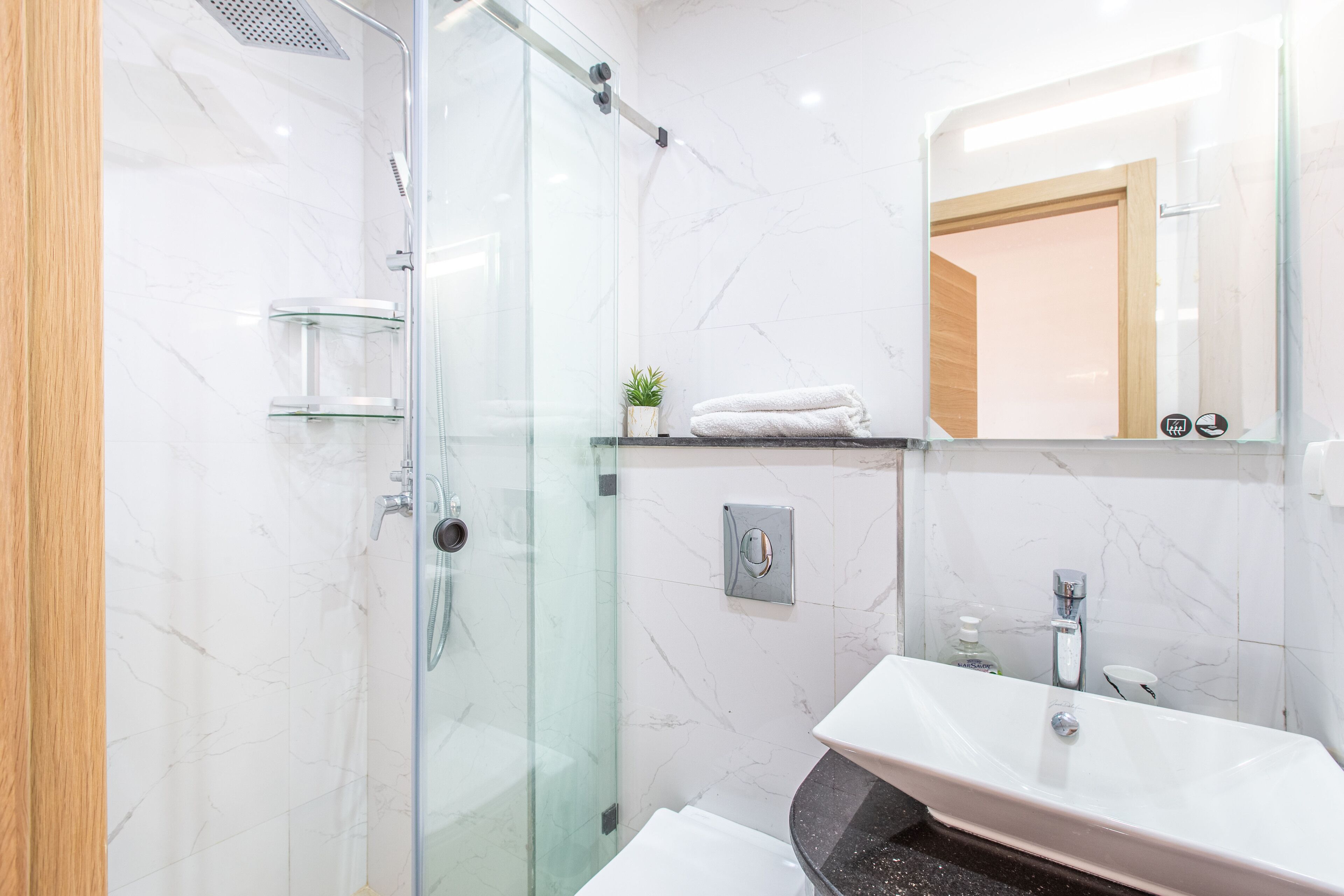 Une salle de bain moderne avec une douche à parois de verre, un lavabo doté d’un plan de travail en marbre et un miroir au-dessus du lavabo.