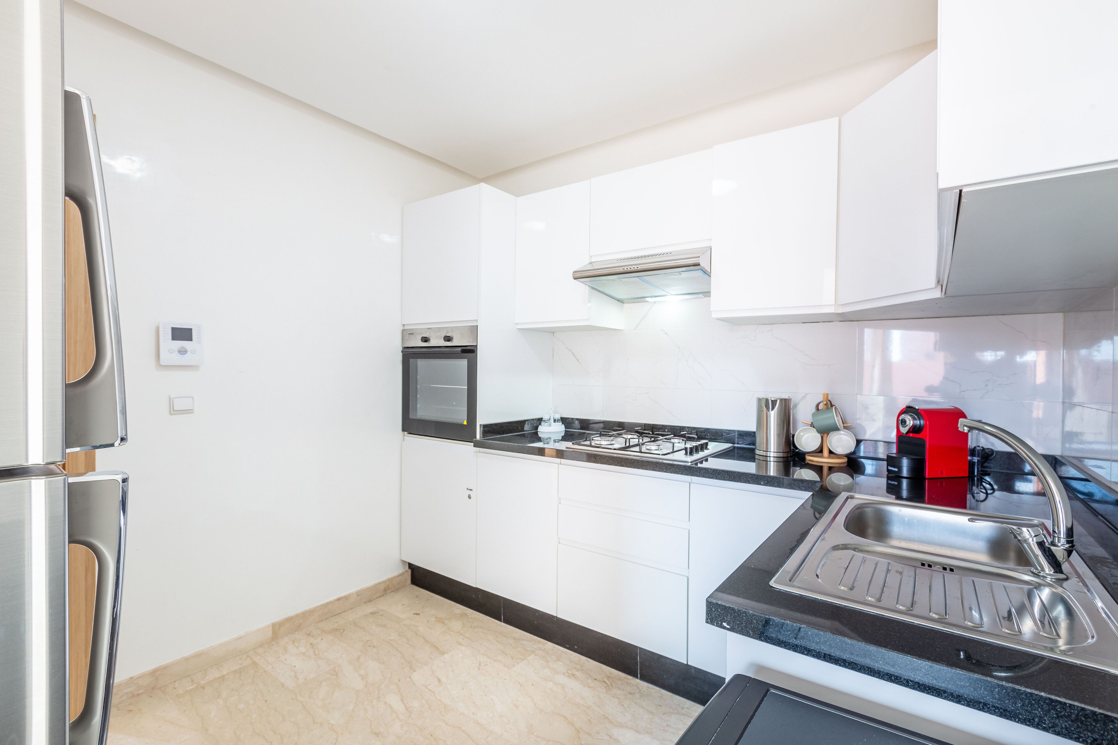 A modern kitchen with white cabinets, a stainless steel refrigerator, a built-in oven, a gas stove, and a sink.