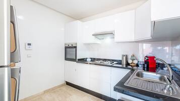 A modern kitchen with white cabinets, a stainless steel refrigerator, a built-in oven, a gas stove, and a sink.