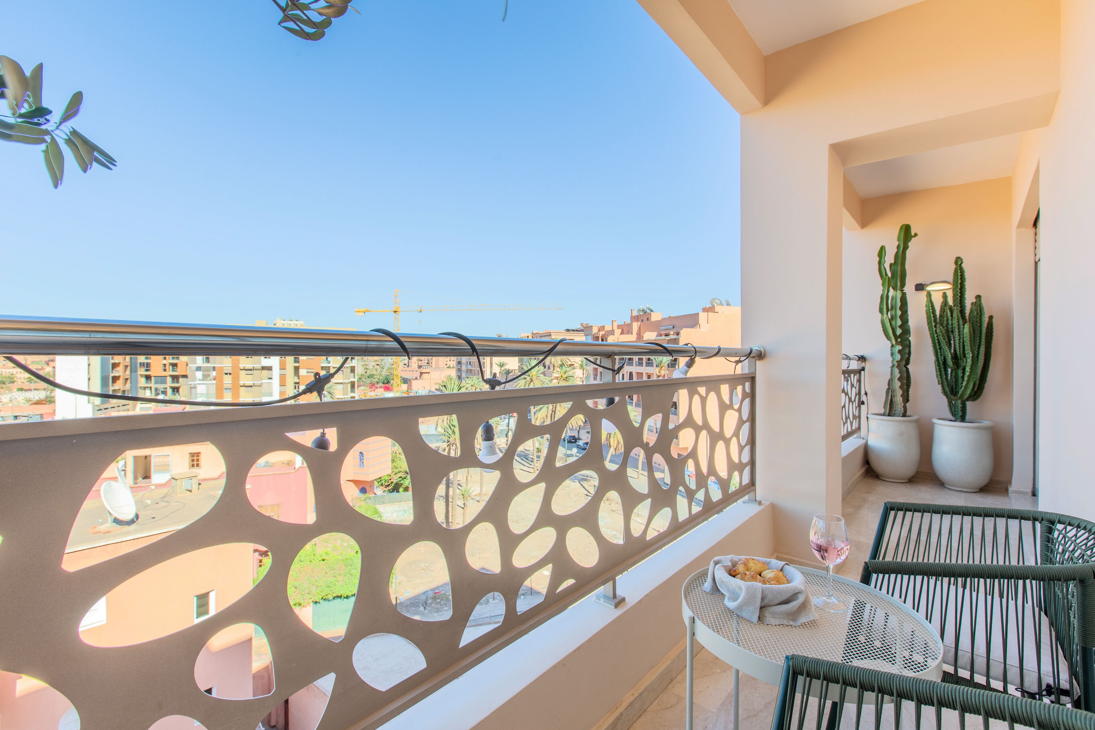 A balcony with a decorative metal railing, a small table with a glass of wine, and two chairs.