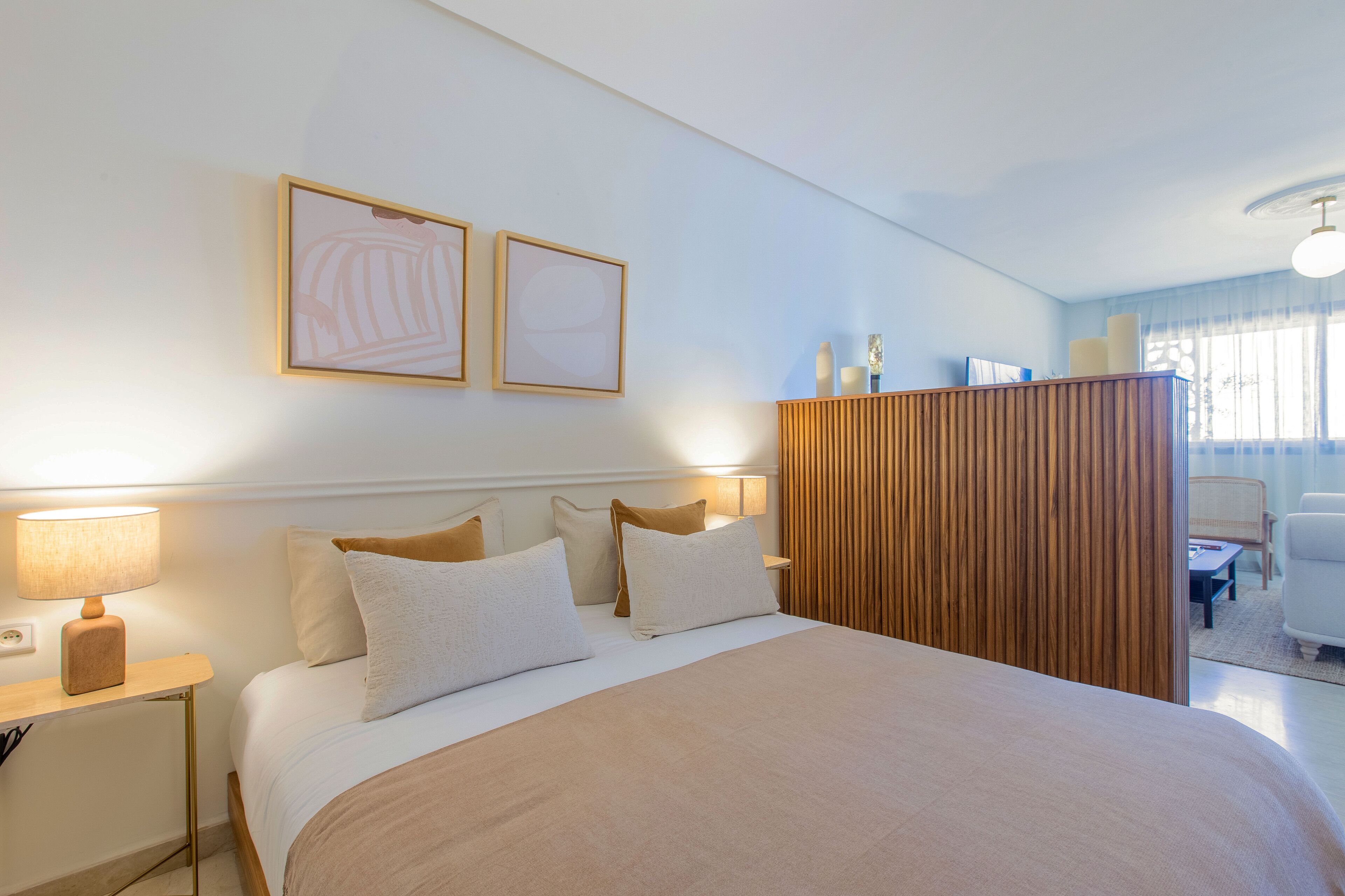 A hotel room with a large bed, bedside tables, a wooden partition, and a view of the outdoors through the window.