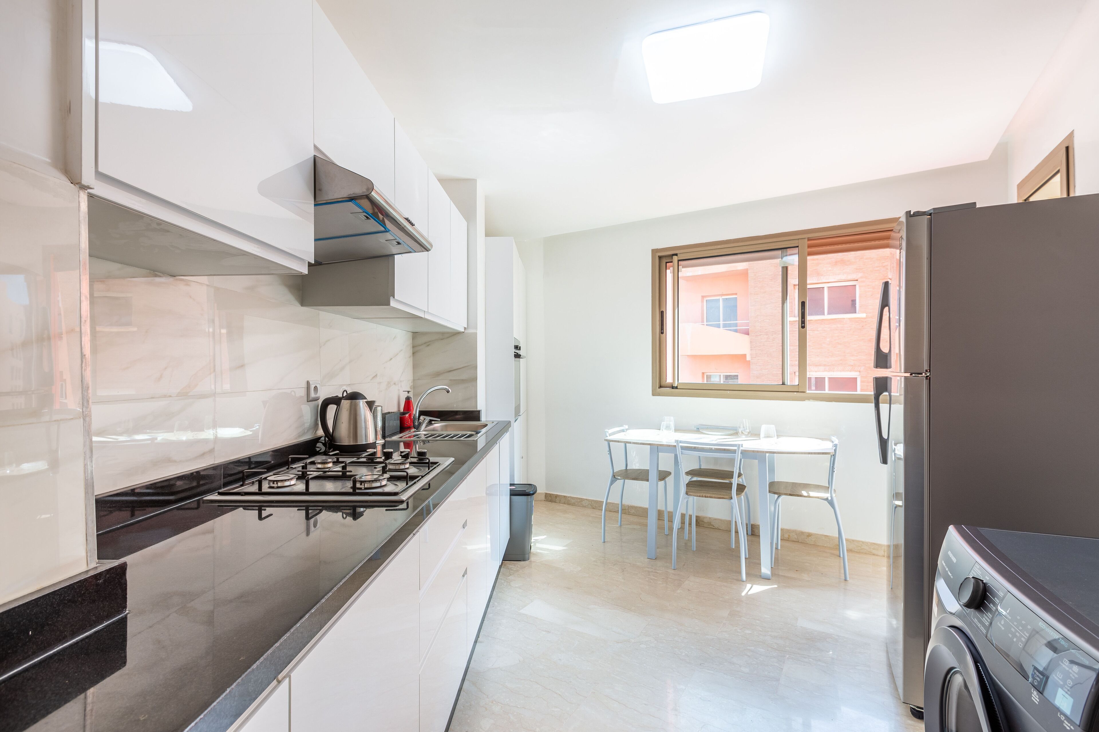 A modern kitchen with white cabinets, a black countertop, a gas stove, and a built-in oven. There is a window with a view of a building outside.