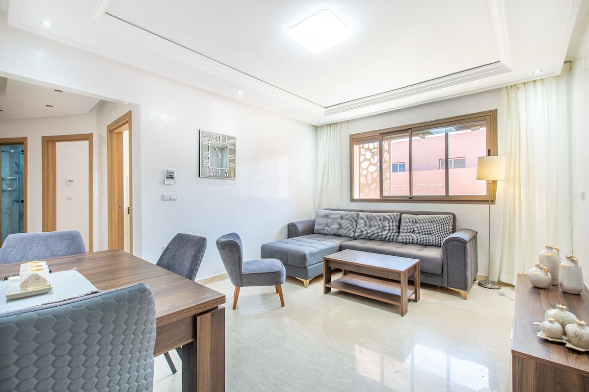 A modern living room with a wooden dining table, grey upholstered chairs, a grey sofa, and a floor lamp.