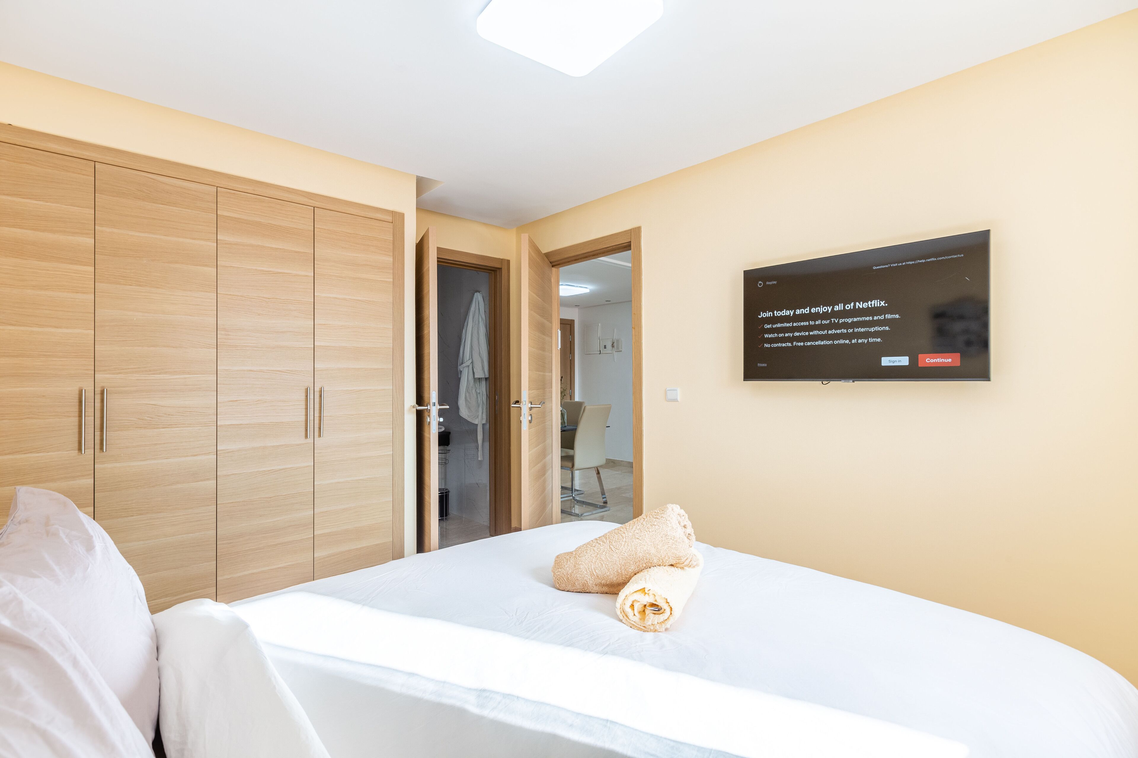 A hotel room with a bed, a wardrobe, a television mounted on the wall, and a bathroom visible through an open door.