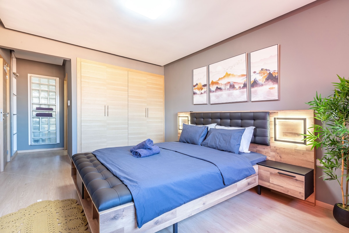Un dormitorio moderno con una cama grande, una mesita de noche, un armario y una obra de arte colgada en la pared.