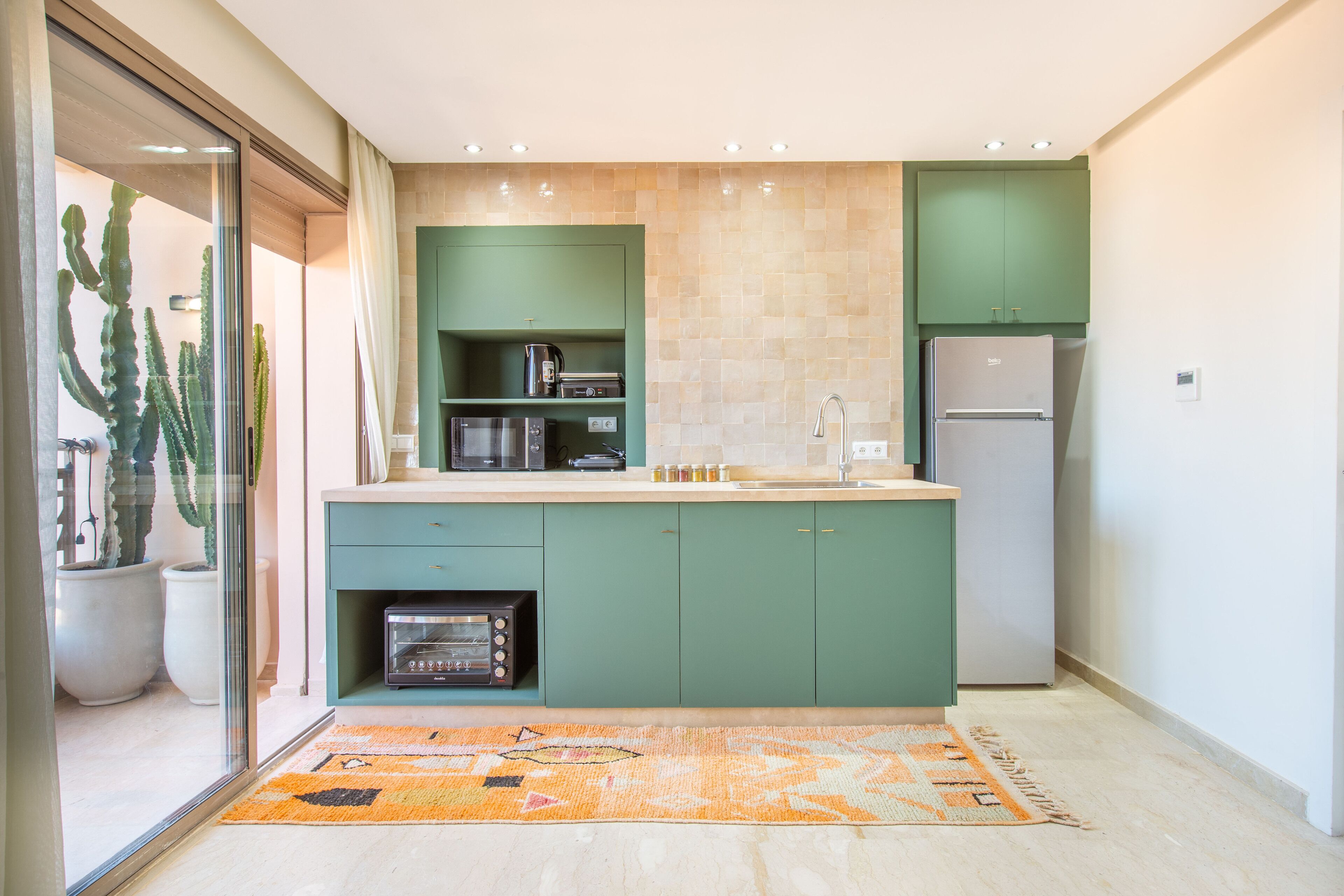 A modern kitchen with green cabinets, a built-in microwave, and a refrigerator.