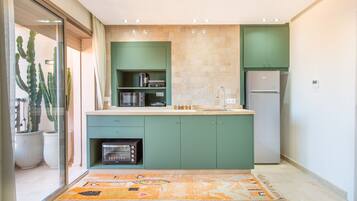 A modern kitchen with green cabinets, a built-in microwave, and a refrigerator.