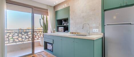 A modern kitchen with a large refrigerator, a sink, and a window overlooking a balcony.
