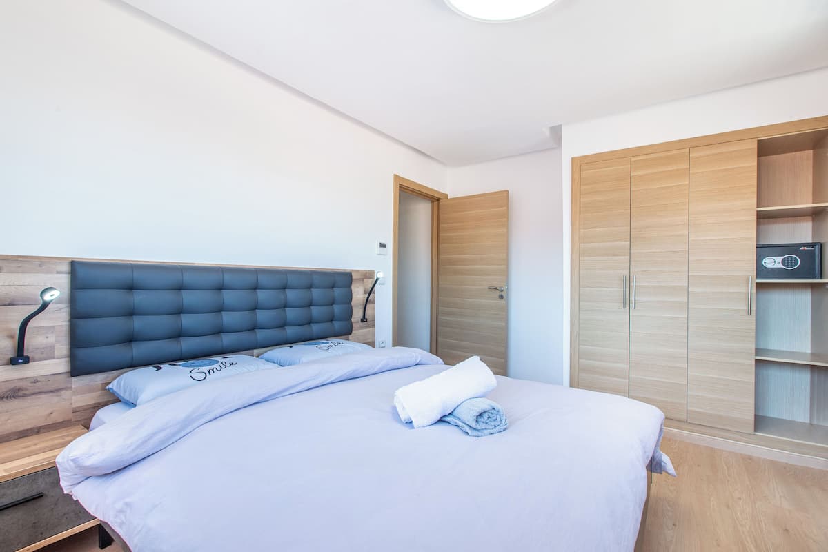 A bedroom with a bed, a wooden wardrobe, and a nightstand with a lamp.