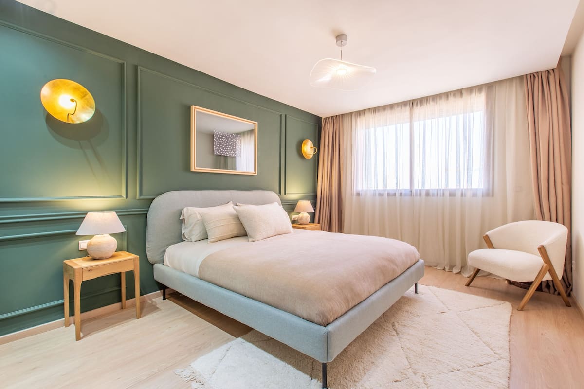 A modern bedroom with a bed, bedside tables, a chair, and a large window with curtains.