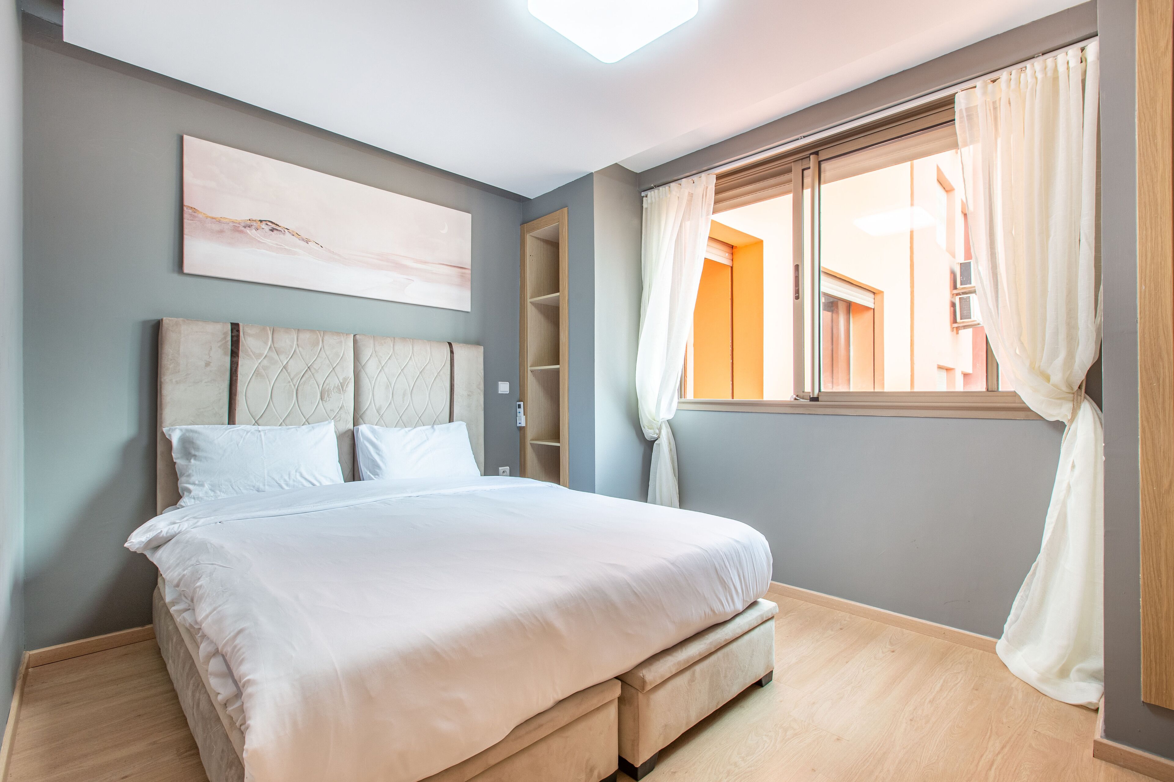 Un dormitorio con cama, ventana con cortinas, lámpara de techo y estante en la pared.