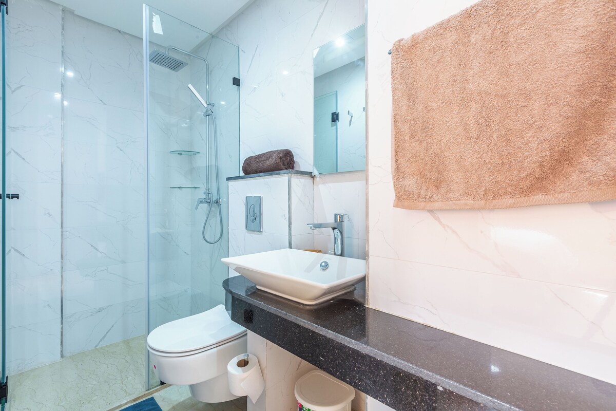 A modern bathroom with a glass shower enclosure, a white sink, and a beige towel.