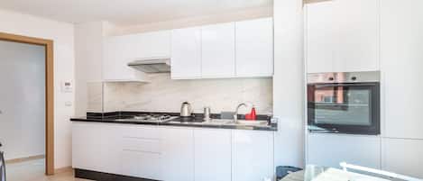 Una cucina moderna con mobili bianchi, un piano di lavoro nero e un forno integrato.
