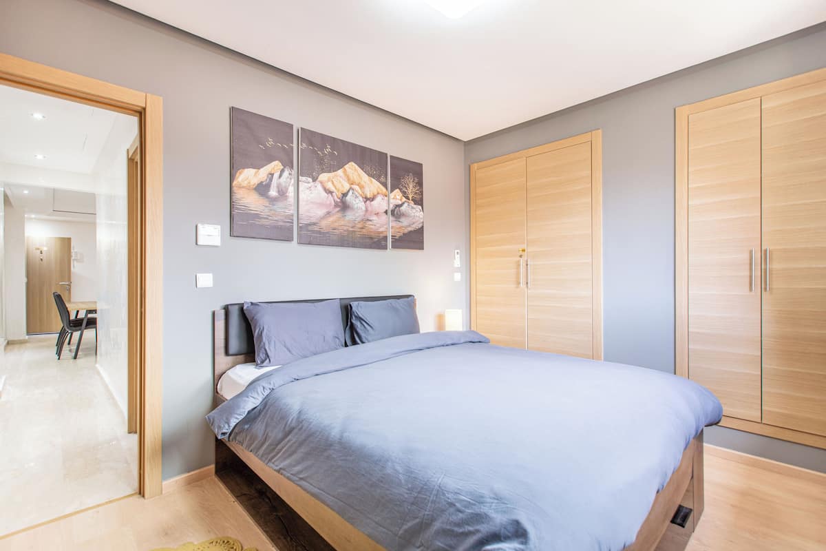 A modern bedroom with a large bed, wooden wardrobe, and a painting on the wall.