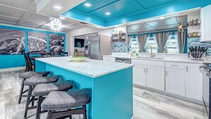 A modern kitchen with a blue accent wall, a central island with bar stools, stainless steel appliances, and a large mural on the wall. - Turquoise Turtle - Private Heated Pool: Relax & Enjoy (Fort Pierce)