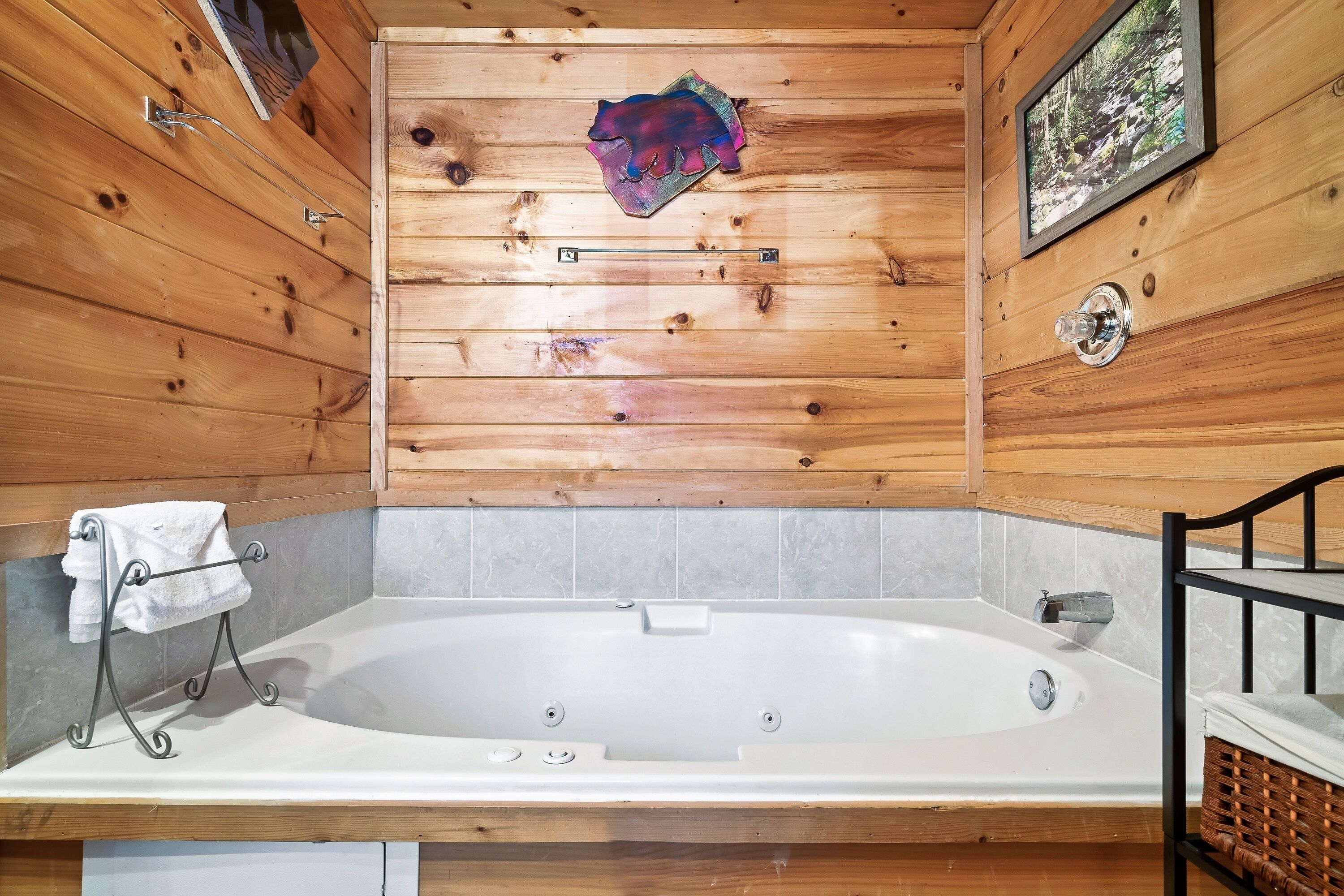 Une salle de bain rustique, avec des murs en bois, une grande baignoire, un porte-serviettes et un tableau encadré accroché au mur.