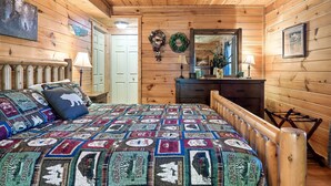 A cozy log cabin bedroom with a wooden bed, a dresser, and a mirror. - A Top Notch Lodge (Gatlinburg)