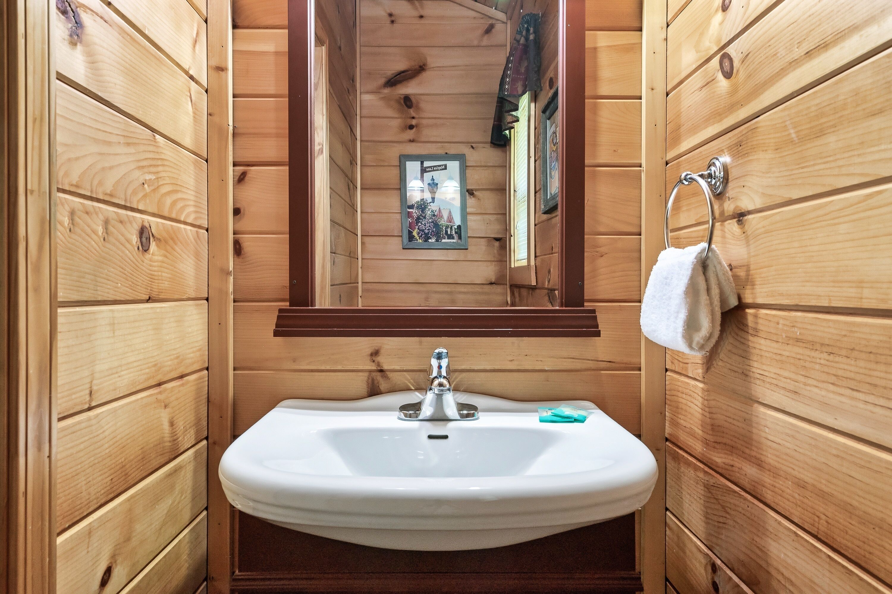 Un baño de cabaña de madera con un lavabo blanco, un espejo y una toalla colgada en un perchero.