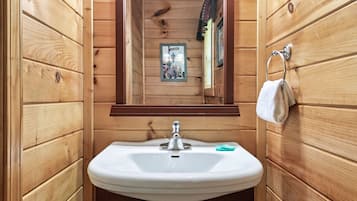 A wooden cabin bathroom with a white sink, a mirror, and a towel hanging on a rack.