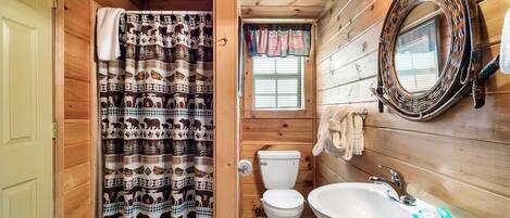 A wooden cabin bathroom with a patterned shower curtain, a toilet, a sink, and a mirror.