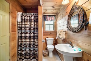 A wooden cabin bathroom with a patterned shower curtain, a toilet, a sink, and a mirror. - A Top Notch Lodge (Gatlinburg)