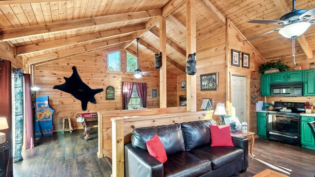 A wooden cabin interior with a black leather sofa, a dining table, and a kitchen area. - A Top Notch Lodge (Gatlinburg)